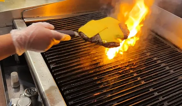 A freshly made burger with melted cheese over a flame grill.