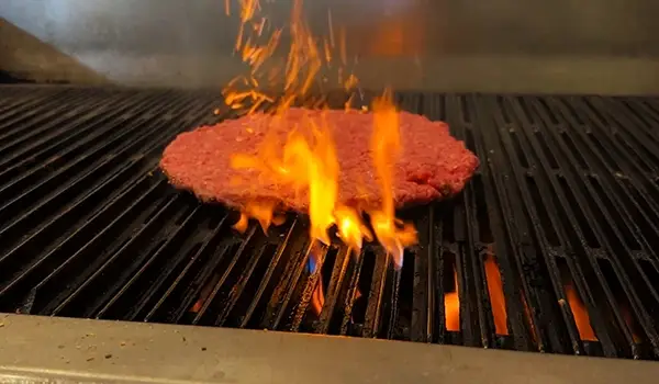 A fresh ground beef burger being flame grilled
