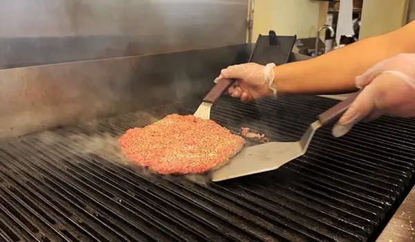 A freshly pattied burger being placed on the grill